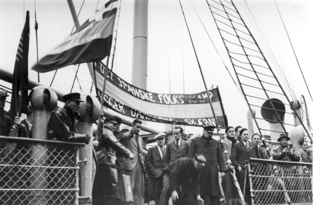 S/S Bernstorffs ankomst til Esbjerg Havn med de 91 frivillige, november 1938. Teksten på banneret er som følger: “I det spanske folks kamp ligger Danmarks skæbne”